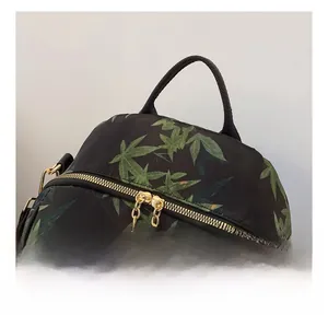 Detail of smooth gold zipper and maple leaf pattern on black fabric backpack