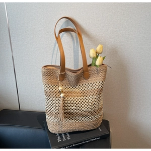 Détail d'un sac cabas en paille tissée avec pompon et longues anses en cuir marron