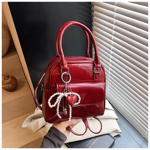 Close-up of red patent leather backpack with pearl bow and heart charm detail