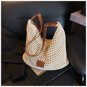 Close-up of cream woven tote bag with brown leather handles on dark background