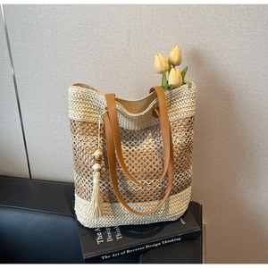 Détail d'un sac cabas en paille avec anses en cuir et pompon sur des livres