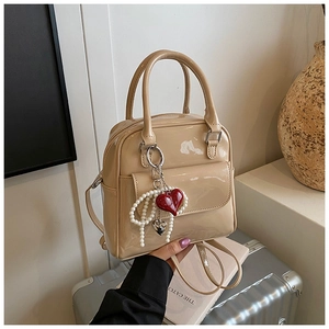 Close-up of beige patent leather bag with heart pearl charm on a silver suitcase