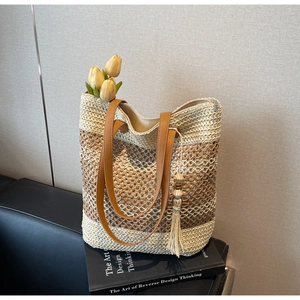 Détail du sac cabas en paille rayé avec poignées en cuir et décor de glands