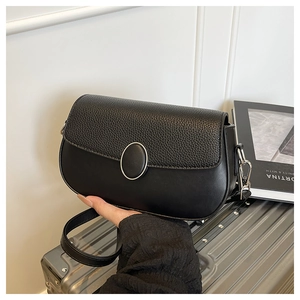 Detail of minimalist black faux leather shoulder bag with buckle on a silver suitcase