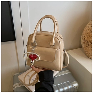 Detail of beige patent leather handbag with pearl heart charm and crossbody strap