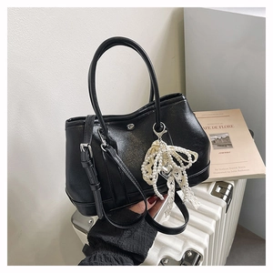Détail d'un sac seau en cuir noir avec élégant pendentif décoratif en perles et dentelle