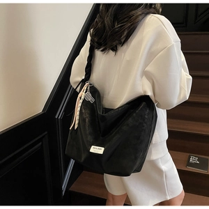 Close-up of black leather tote bag featuring a woven strap and mini tennis racket charm