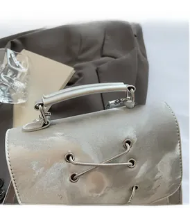 Detail of silver metallic handbag featuring cross-strap design and sturdy round handle