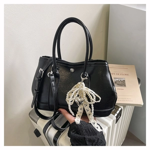 Détail d'un sac seau en cuir grainé noir avec un accessoire de perles et un nœud en dentelle