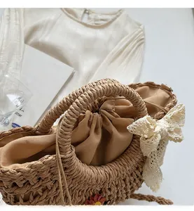 Close-up of straw woven bag featuring white lace bow, red flower and drawstring liner