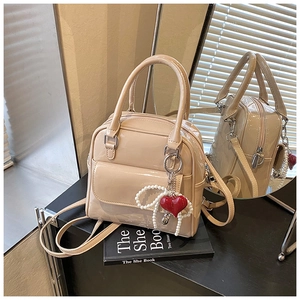 Detail of beige patent leather mini backpack featuring heart pearl charm and glossy finish
