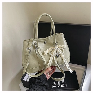 Détail d'un sac seau vert clair avec nœud en dentelle, pompons perlés et charme cœur