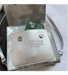 Detail of silver metallic crossbody bag showing front pocket capacity with a smartphone