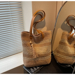 Détail d'un sac cabas en paille tissée avec anses en cuir marron et breloque à pompon en bois