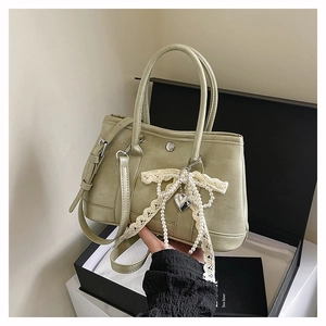Détail du sac seau vert avocat avec nœud en dentelle, perles et pendentif en cœur