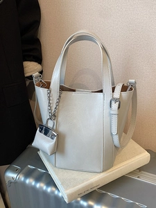 Elegant beige trapezoid bucket bag with top handles and adjustable strap on luggage