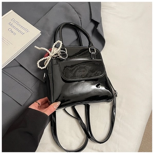 Detail of black patent leather crossbody bag with a pearl bow charm and high gloss finish