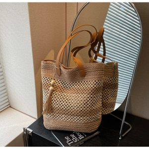 Détail du sac cabas en paille montrant le tissage ajouré et le pompon en cuir