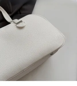 Detail shot of white lychee grain leather texture and metallic buckle on women handbag