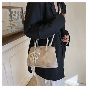 Détail du sac seau structuré beige avec élégant nœud en dentelle et perles raffinées