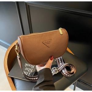 Detail of brown pebbled leather crescent bag with gold zipper and woven wide shoulder strap