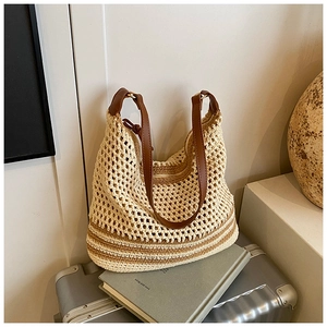 Detail of crochet knit tote bag with brown leather straps on a minimalist silver suitcase