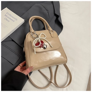 Detailed view of beige glossy leather mini backpack with pearl bow and heart charms
