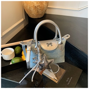 Detail of blue denim mini bag with silver bow and metallic star pendant on black display