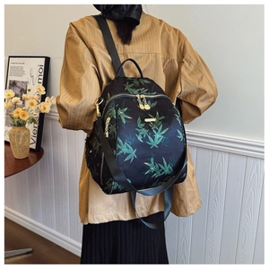 Detail of waterproof black backpack featuring green leaf patterns and gold metal zippers