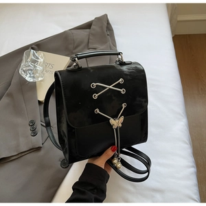 Détail d'un sac à dos en similicuir noir avec pendentif papillon et perle décorative