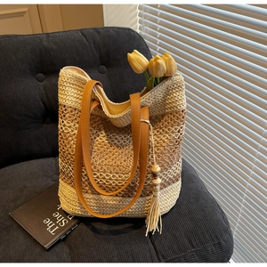 Détail du sac cabas en paille rayé avec anses en cuir marron et pompon décoratif