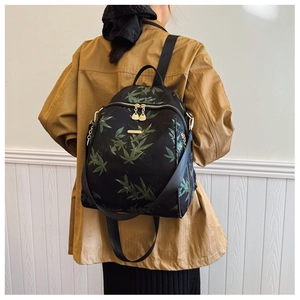 Detail view of a black backpack with green leaf prints on a female model back