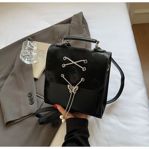 Détail du sac en cuir noir avec boucle papillon argentée et décor de franges en perles