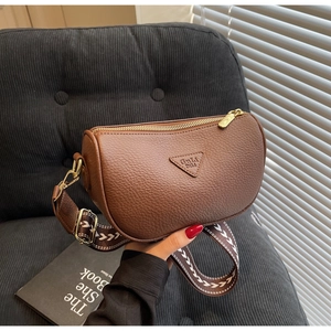 Detail of brown leather pillow bag featuring a wide woven strap and golden hardware