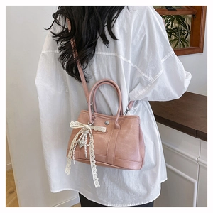 Sac seau en cuir rose avec nœud en dentelle blanche et perles porté par modèle