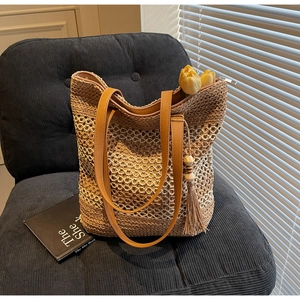 Détail du sac cabas en paille avec motif de tissage ajouré et pompon décoratif en perles de bois