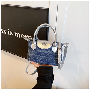 Detail of denim handbag with silver flap, metallic bow, and adjustable shoulder strap