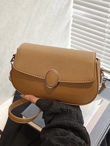 Minimalist brown pebbled leather crossbody bag with metal buckle in soft sunlight