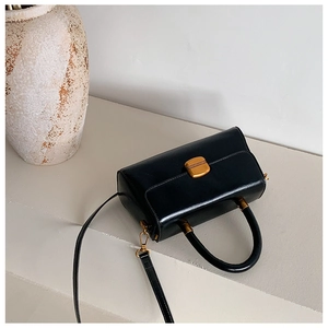 Detail einer schwarzen Ledertasche mit strukturiertem goldenem Metallschloss und Griff