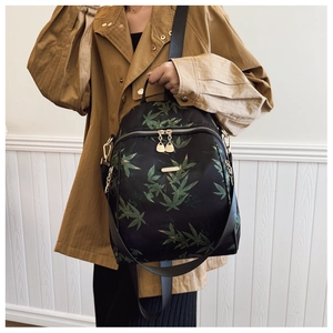 Detailed view of the stylish black backpack featuring green bamboo leaf patterns and gold metal logo