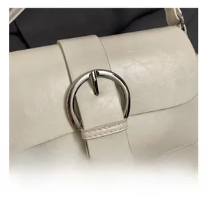 Detail shot of the large silver circular buckle and creamy white leather texture on the bag