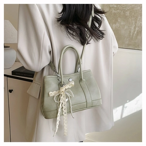 Détail du sac seau vert clair avec nœud en dentelle et perles porté par un modèle