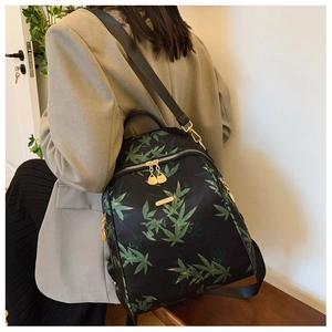 Detail of fashion backpack featuring green leaf print and golden zippers on model