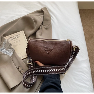 Detail of dark brown pebble leather pillow bag with stylish wide woven strap and gold hardware