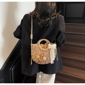 Detail of straw woven bag featuring 3D daisies and a lace bow on a crossbody strap