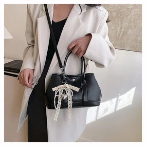 Détail du sac seau en cuir noir avec bordure en dentelle blanche et breloque perle