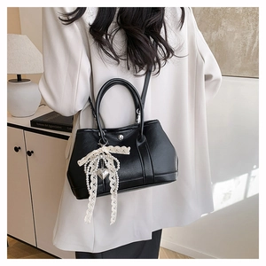 Détail du sac seau noir avec pendentif nœud en dentelle et breloque en forme de cœur argenté