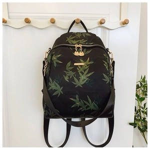 Close-up of black backpack featuring green bamboo leaf prints and golden metal zippers
