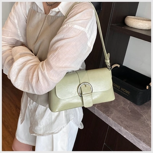 Detail of light green underarm bag featuring a metallic silver circular buckle closure