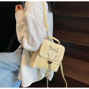 Détail du sac à dos en cuir beige brillant avec breloque nœud et pompon de perles